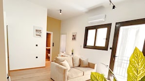 Ein geräumiges Wohnzimmer mit einem beigen Sofa, einer großen Topfpflanze und einer Deckenleuchte.
