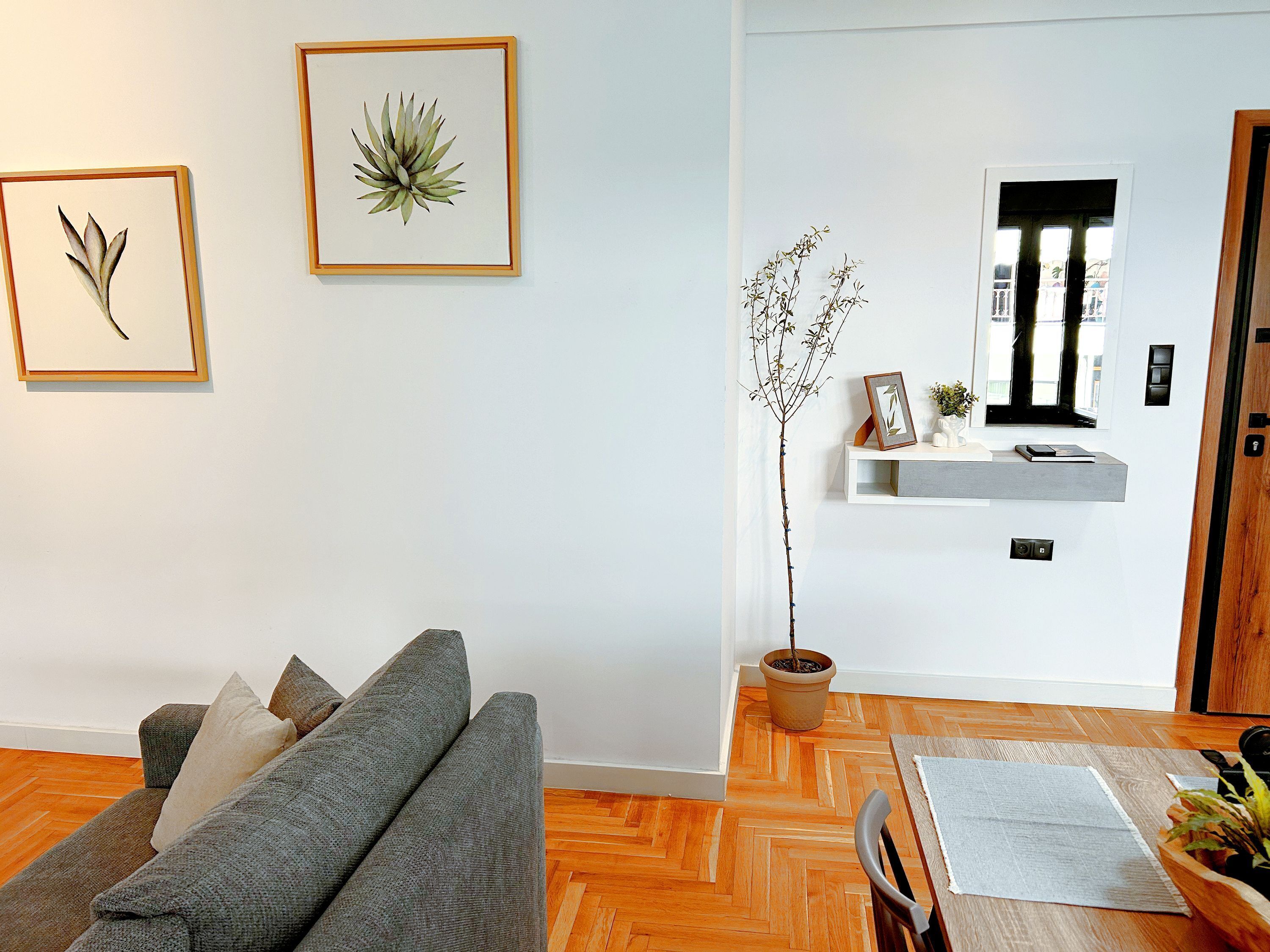 Una sala de estar con un sofá gris, piso de madera y una planta en maceta.