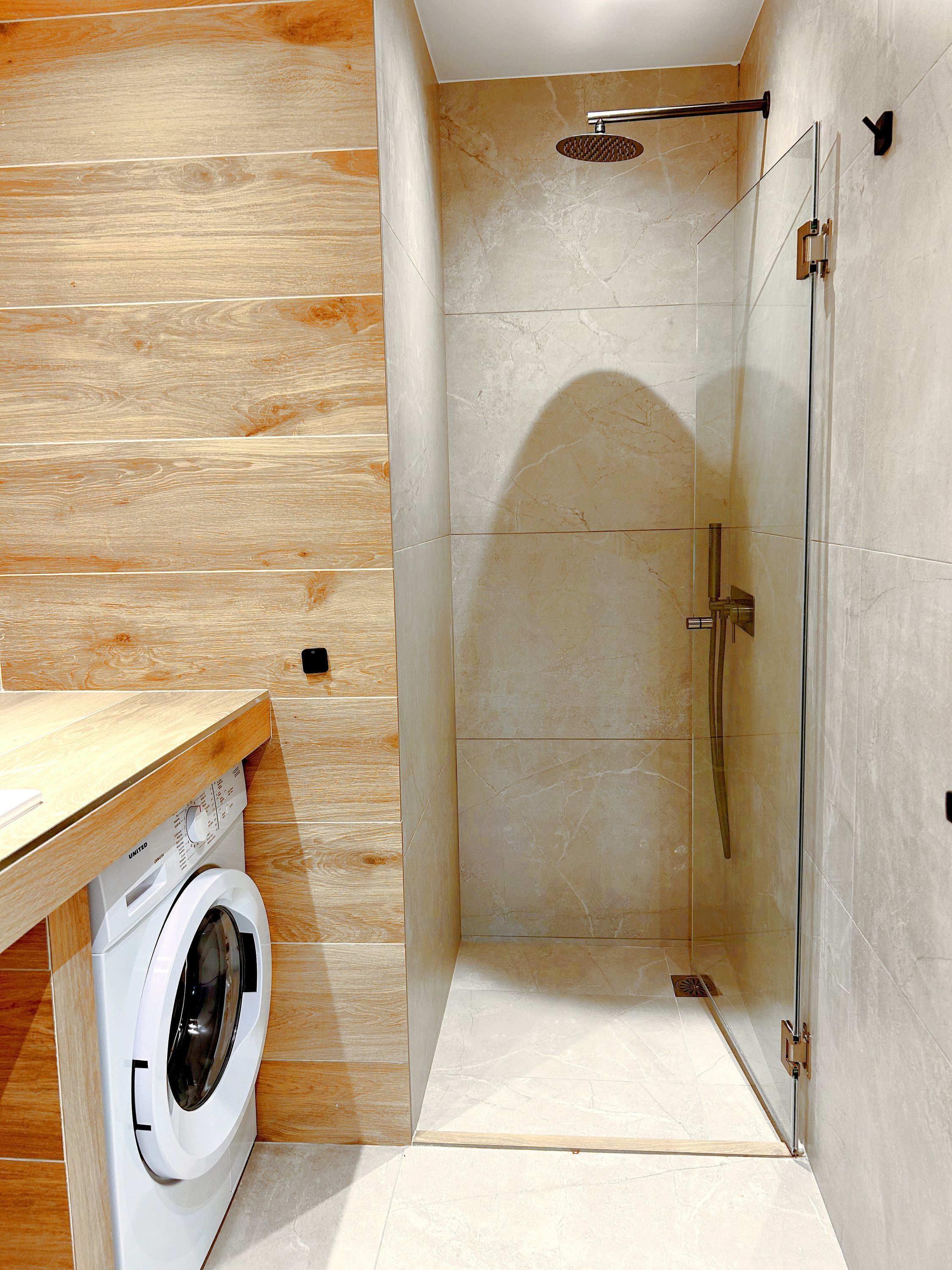 Een moderne badkamer met een houten wastafelmeubel, een ingebouwde wasmachine en een douchecabine met glazen wanden.