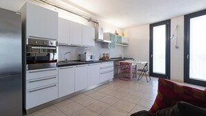 A modern kitchen with white cabinets, stainless steel appliances, and a dining area with a table and chairs. - Italianway Easy - Segesta 3 (San Siro)