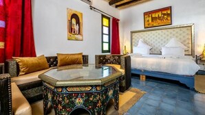 A room with a bed, a sofa, a glass-top coffee table, and a patterned ottoman. - Kasbah Lilas sleeps 46 (Douar Akkara)