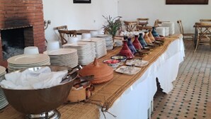A long dining table set with plates, bowls, and decorative items, with a brick fireplace and hanging baskets in the background. - Kasbah Lilas sleeps 46 (Douar Akkara)