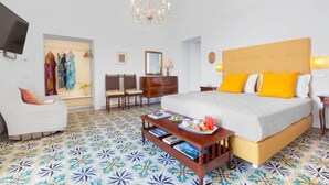 A hotel room with a large bed, a wooden nightstand, a TV, a chandelier, and a patterned floor. - Mimosa Room Sea View (Torre Elisabetta) (Massa Lubrense)