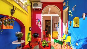 A vibrant patio area with a red and yellow wall, a small table with a potted plant, and a grill. - Magma Loft by NapoliApartments (Naples)