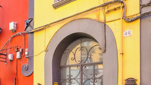 A building with a yellow and orange facade, a metal gate with decorative patterns, and a cobblestone street. - Magma Loft by NapoliApartments (Naples)