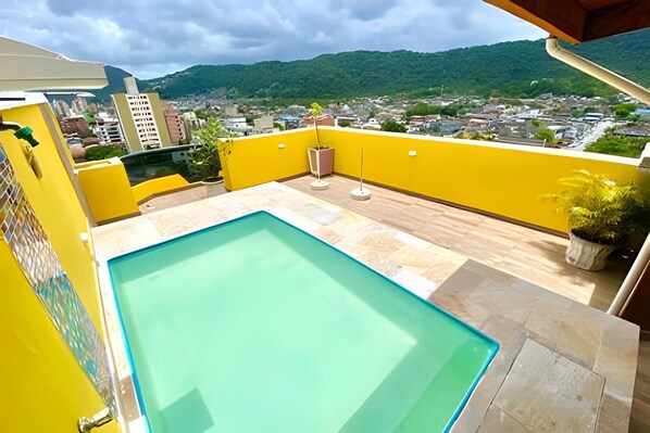 Una piscina en la azotea con vistas a un paisaje urbano y montañas al fondo.