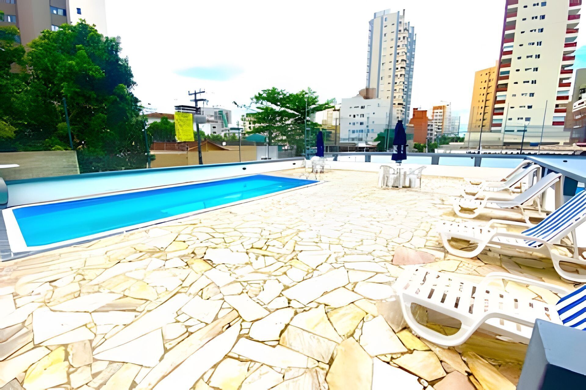 A rooftop pool with stone flooring, lounge chairs, and a view of the cityscape.
