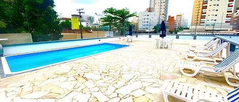 A rooftop pool with stone flooring, lounge chairs, and a view of the cityscape.