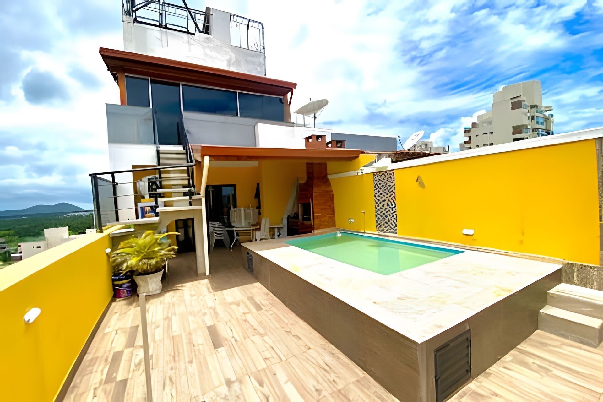A modern rooftop with a swimming pool, a staircase, and a view of the surrounding landscape.