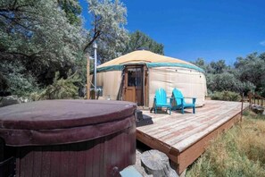 Experience serene tranquility in this traditional yurt, set amidst a forested landscape with a hot tub on the wooden deck.