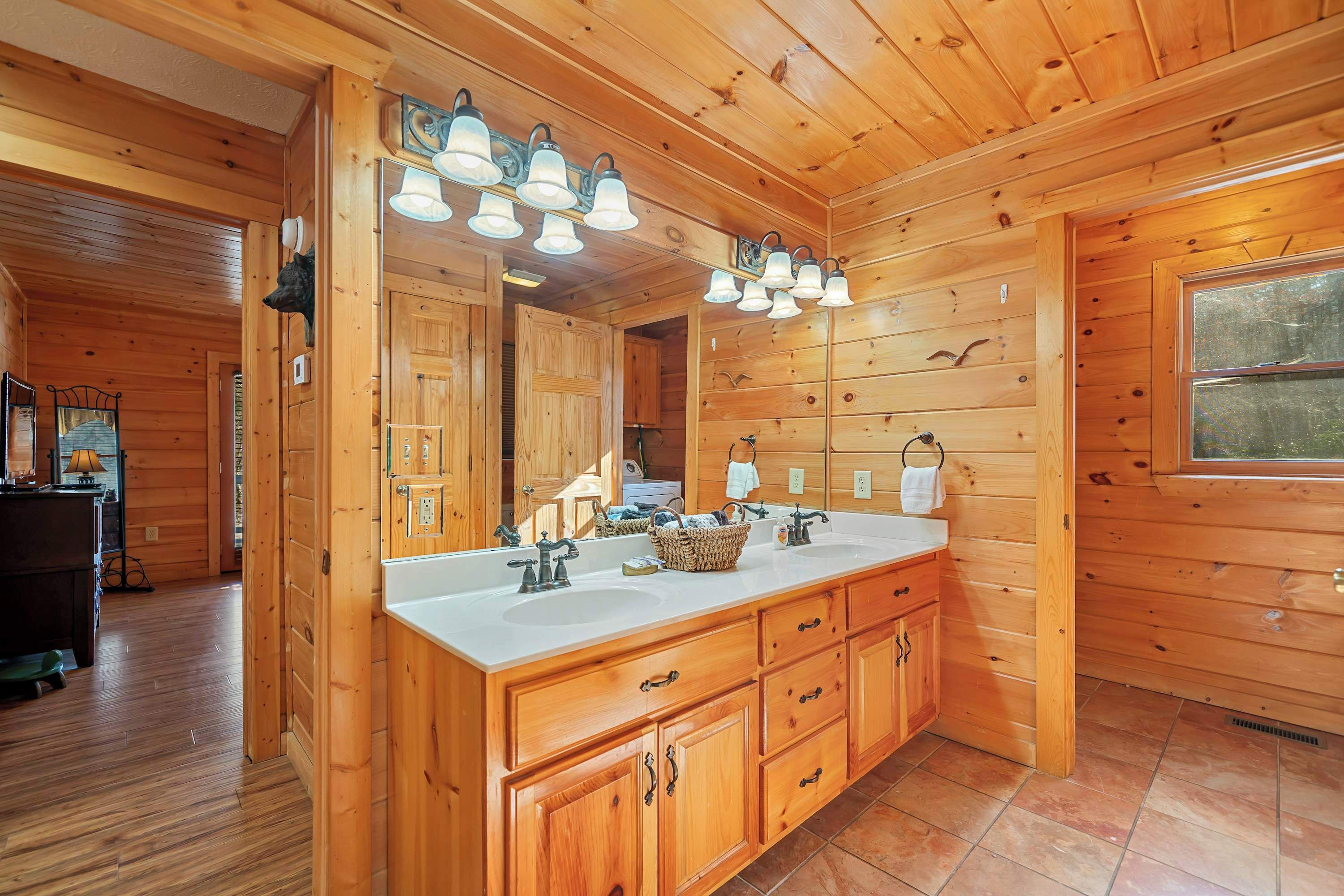 Une salle de bain rustique, avec des murs en bois, un grand miroir, deux vasques et une fenêtre.