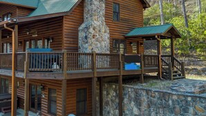 A log cabin with a stone chimney, a balcony, and a stone wall. - New! Riverfront Retreat Sleeps 12 Ellijay (Ellijay)