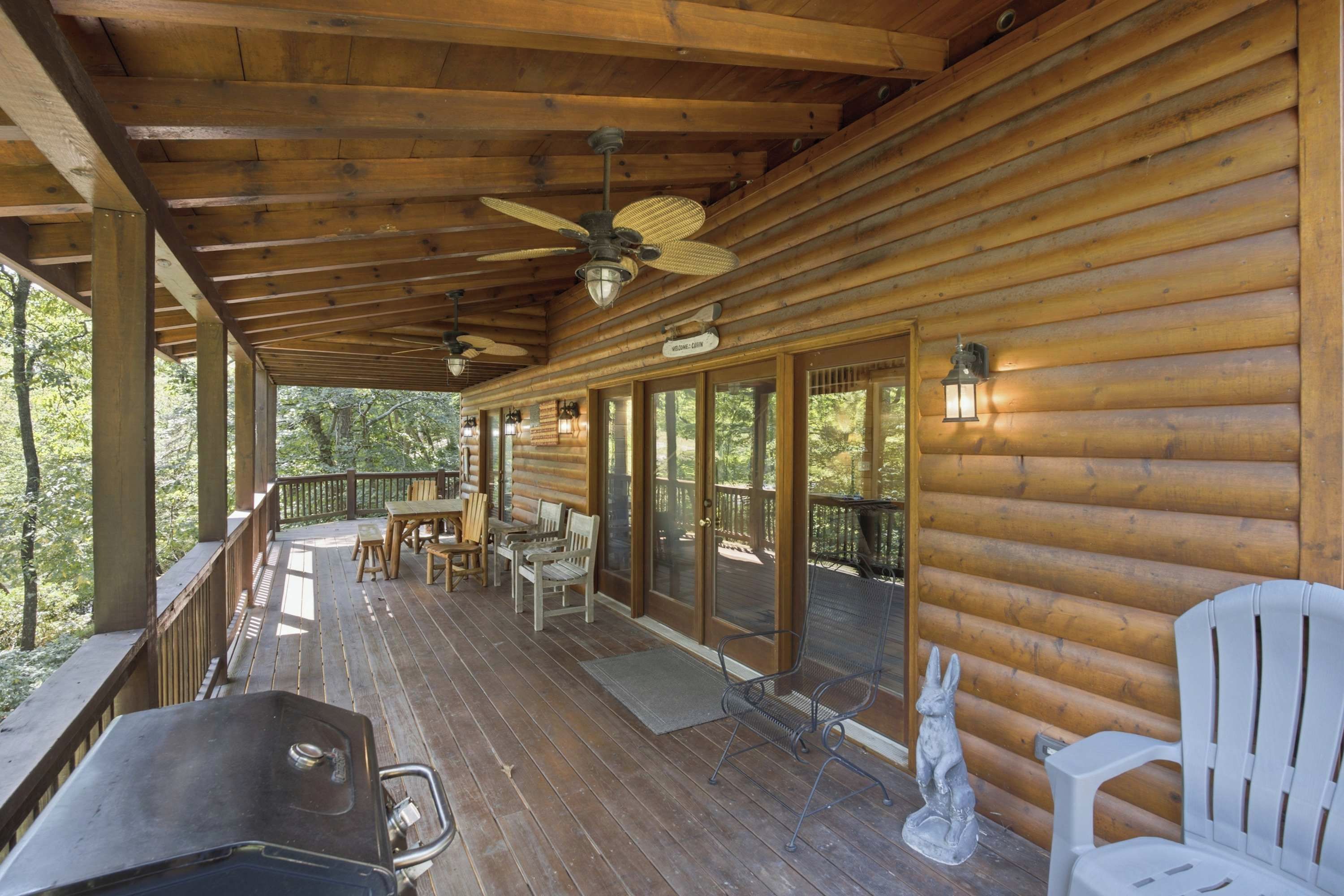 A covered wooden deck with a table and chairs, a statue, and a sign reading 'Welcome - Cabin'.