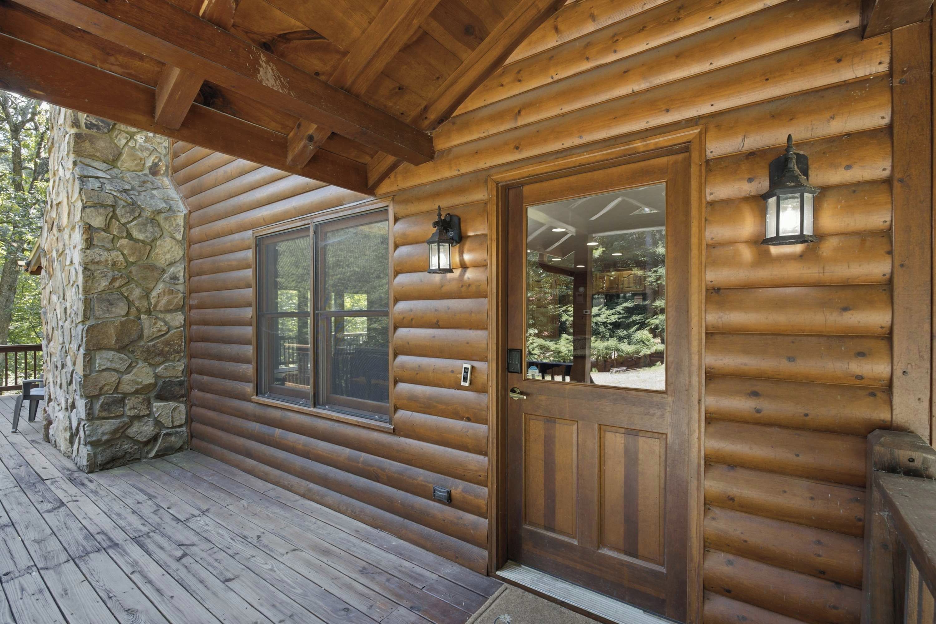 Une cabane en bois avec des fondations en pierre, une terrasse en bois et une porte en verre dotée d’une sonnette et d’un luminaire placé au-dessus.