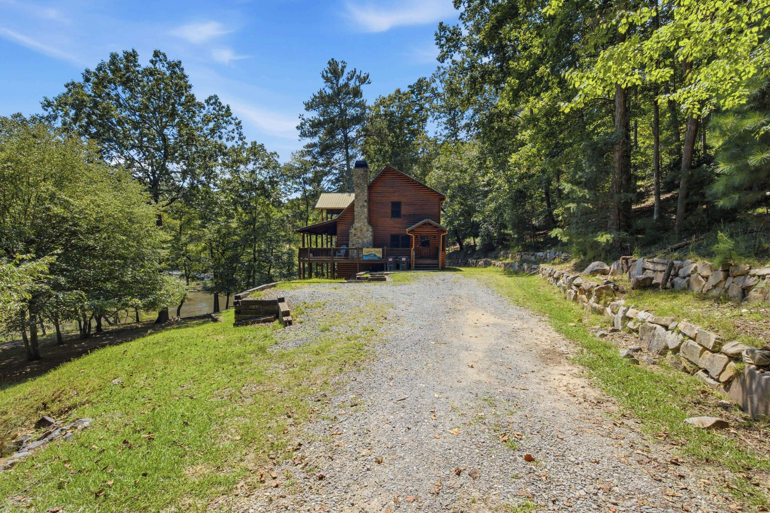 A rustic cabin with a gravel driveway leading to a wooden deck.
