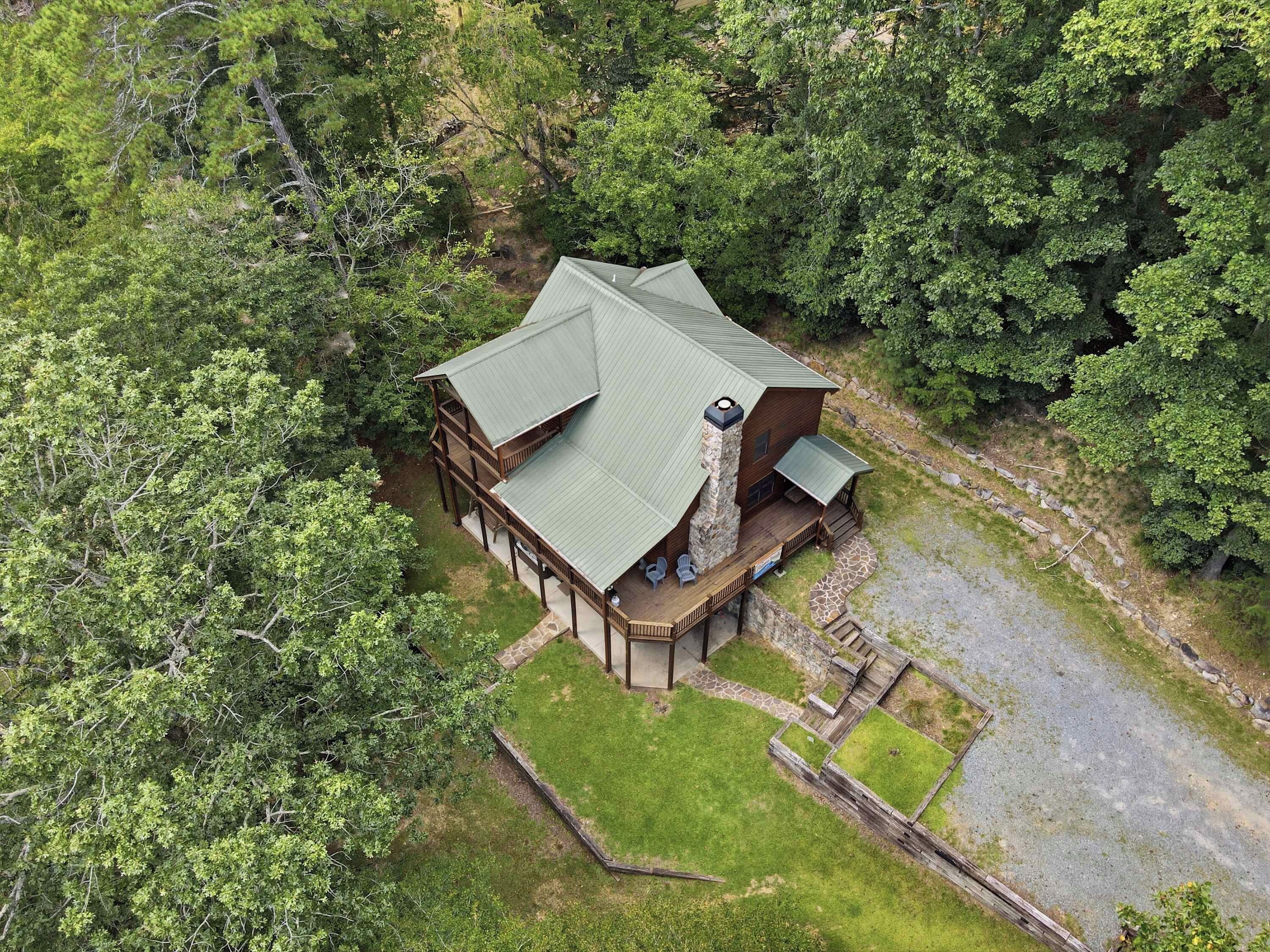 A two-story log cabin with a stone chimney, surrounded by dense forest.