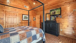 A wooden cabin bedroom with a bed, a dresser, a television, and a ceiling fan. - New! Riverfront Retreat Sleeps 12 Ellijay (Ellijay)
