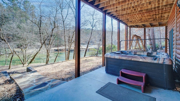 A hot tub in a covered outdoor area with a view of trees and a river. - New! Riverfront Retreat Sleeps 12 Ellijay (Ellijay)