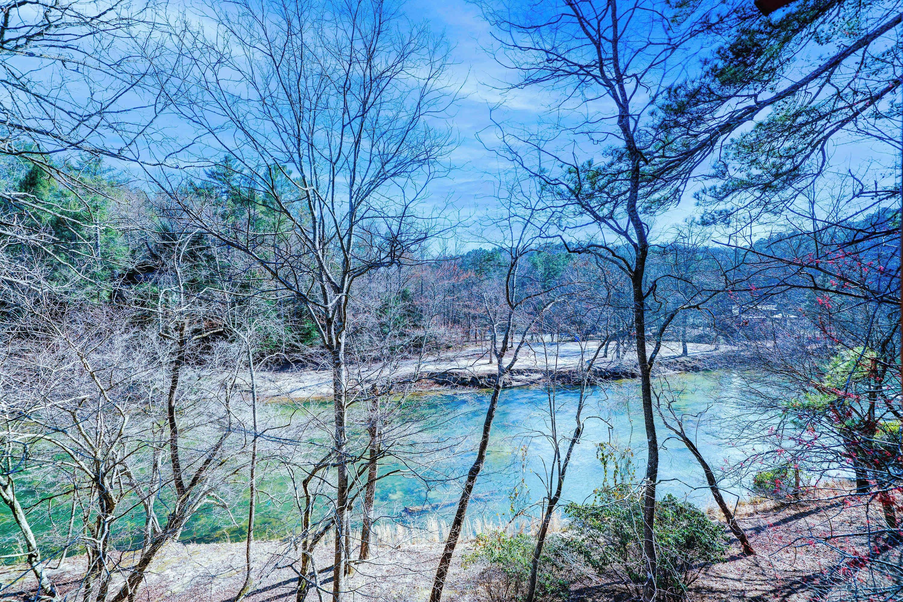 A natural landscape with a river, trees, and a hilly background.