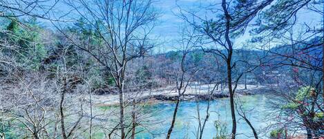 A natural landscape with a river, trees, and a hilly background.