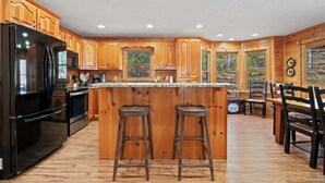 A kitchen with wooden cabinets, a black refrigerator, a microwave, and a bar area with stools. - New! Riverfront Retreat Sleeps 12 Ellijay (Ellijay)