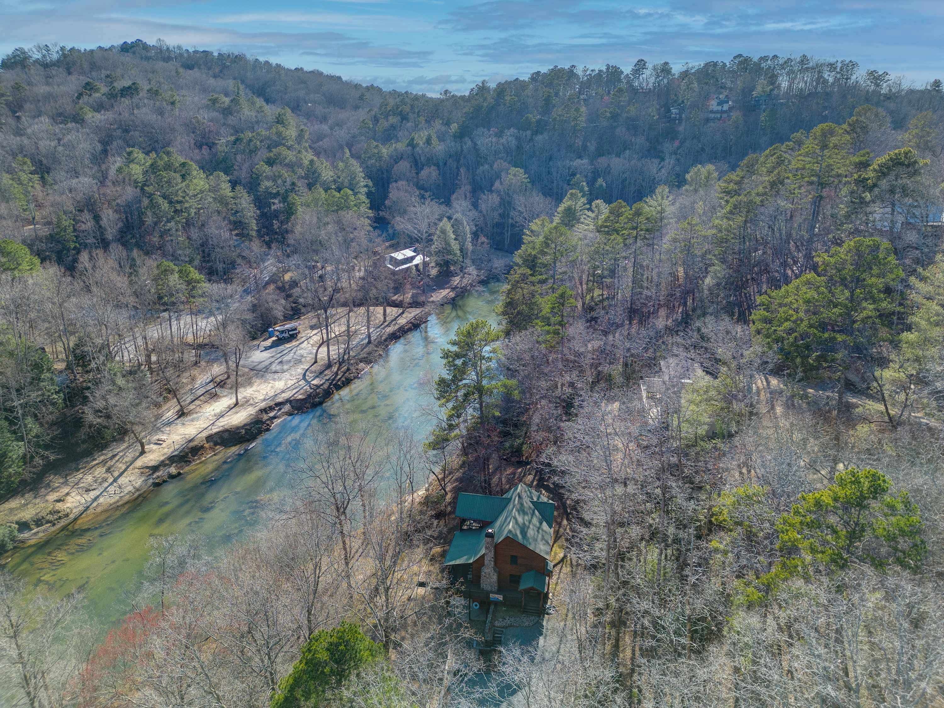 Una baita dal tetto verde, immersa in una fitta foresta e con un fiume nelle vicinanze.