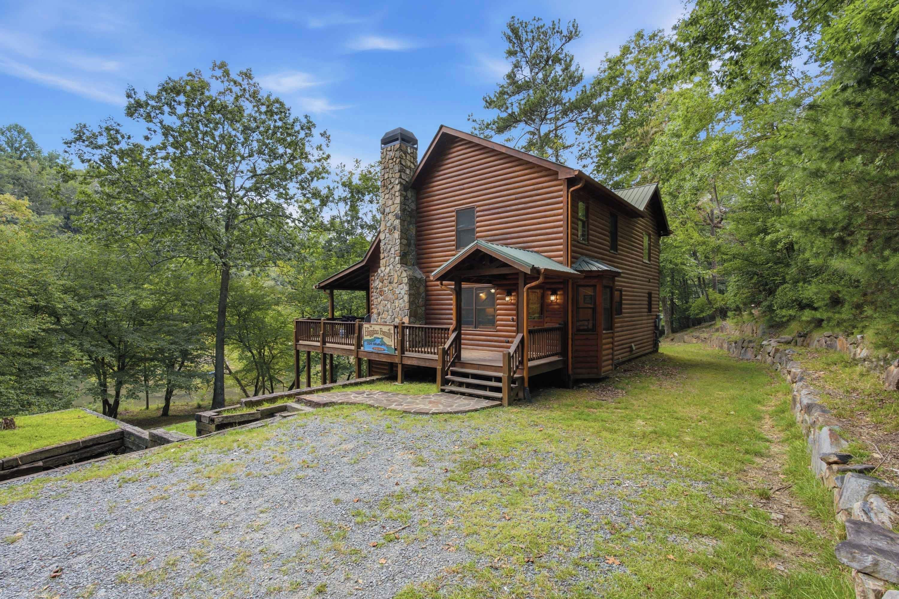 A wooden cabin with a stone chimney, a porch, and a gravel driveway.
