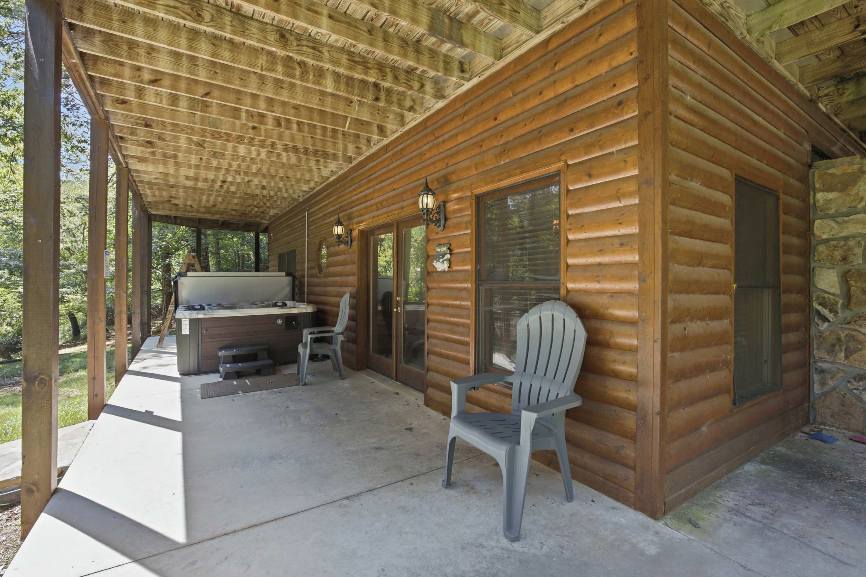 A wooden cabin with a covered patio, a grill, and a chair.