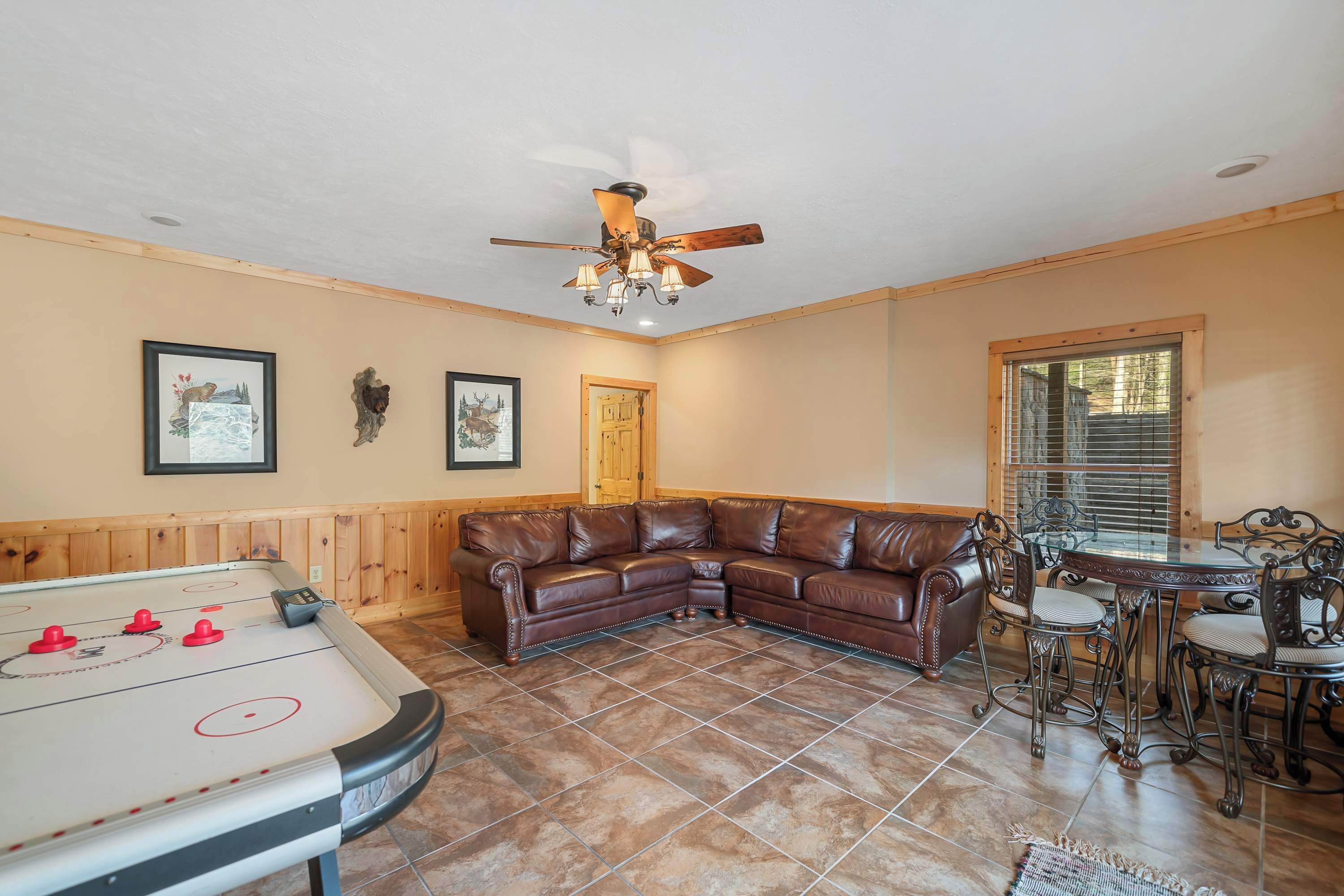 A room with a pool table, a brown leather couch, a dining table with chairs, and a ceiling fan.