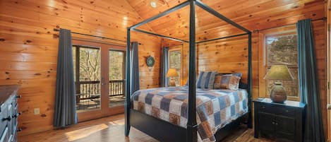 A wooden cabin bedroom with a four-poster bed, a ceiling fan, and a window with curtains.