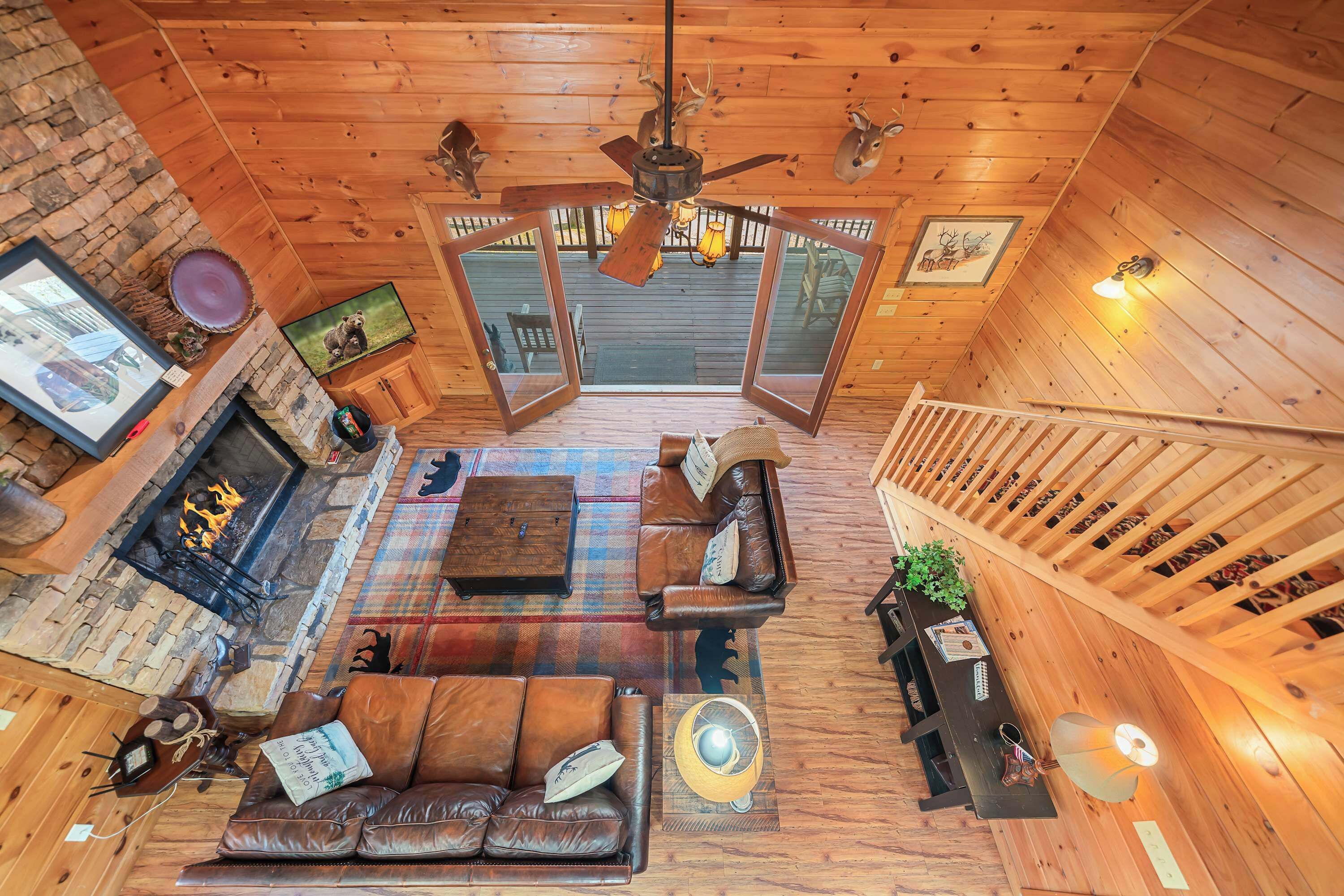 A cozy cabin interior with a fireplace, leather sofa, wooden ceiling, and a staircase.