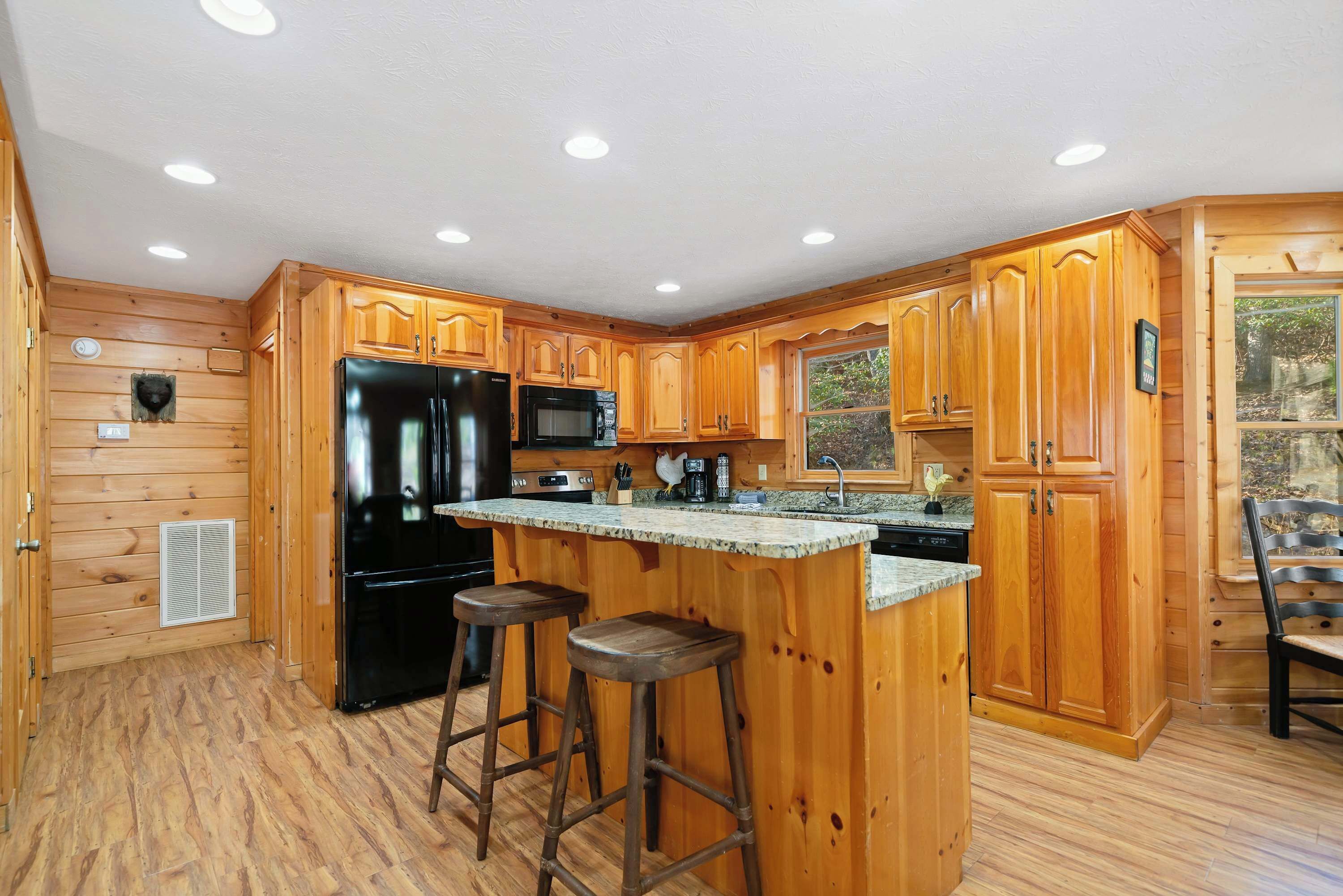 A kitchen with wooden cabinets, a black refrigerator, a microwave, and a granite countertop.
