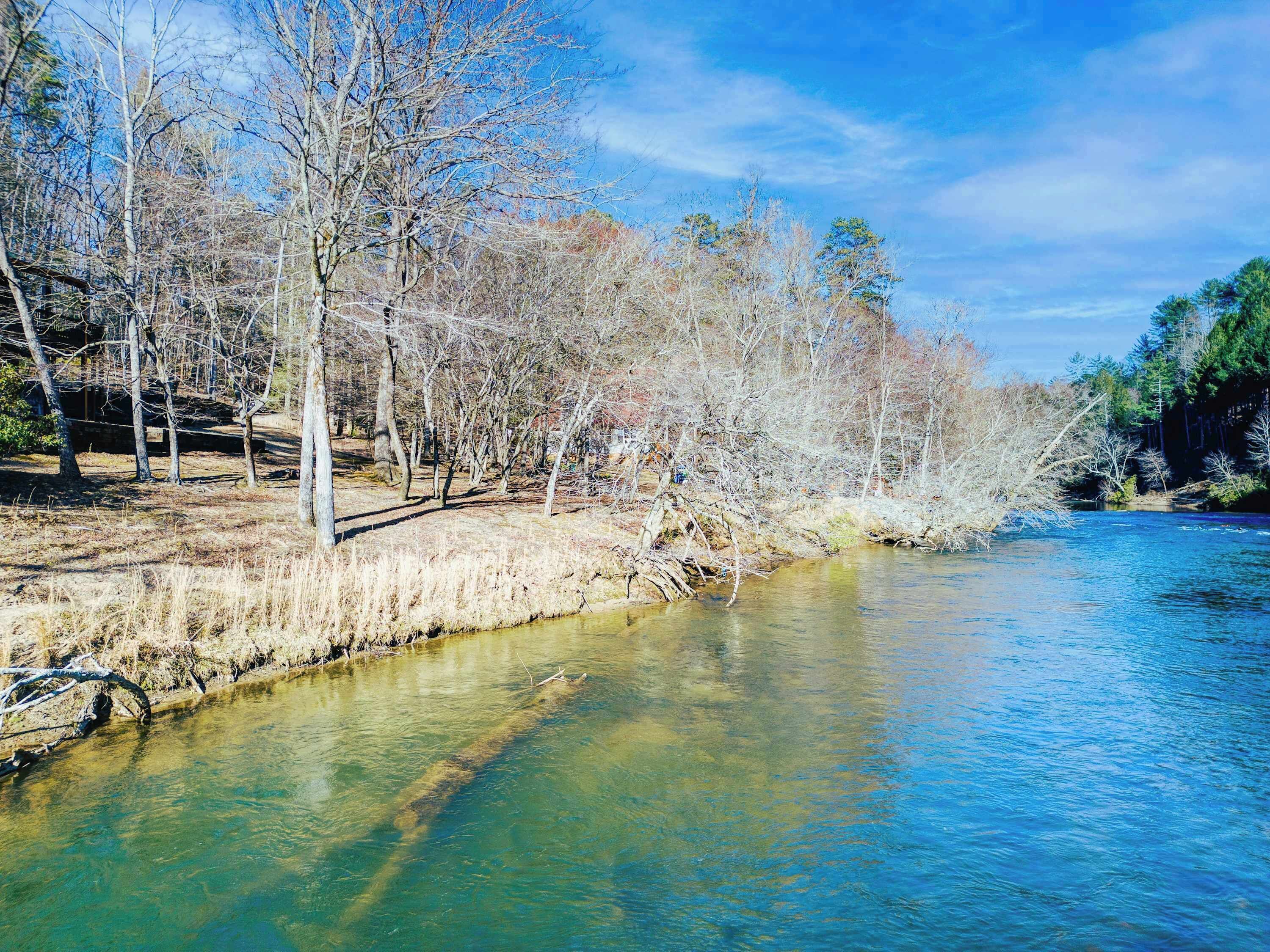 Un río de aguas cristalinas, rodeado de árboles y un puente de piedra.