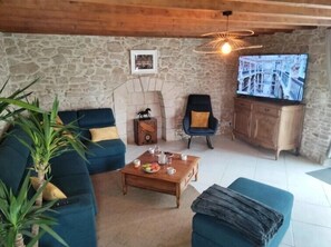 A cozy living room with a stone wall, a blue sofa, a wooden coffee table, and a television. - Manoir de l'Aisnerie (Saint-Herblain)