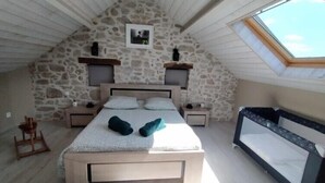 A bedroom with a stone wall, a bed with pillows, a nightstand, a wooden chair, and a skylight. - Manoir de l'Aisnerie (Saint-Herblain)