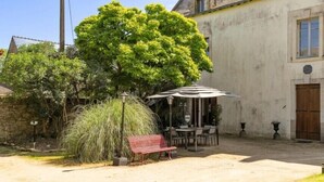 A courtyard with a dining area, a red bench, and a large tree. - Manoir de l'Aisnerie (Saint-Herblain)