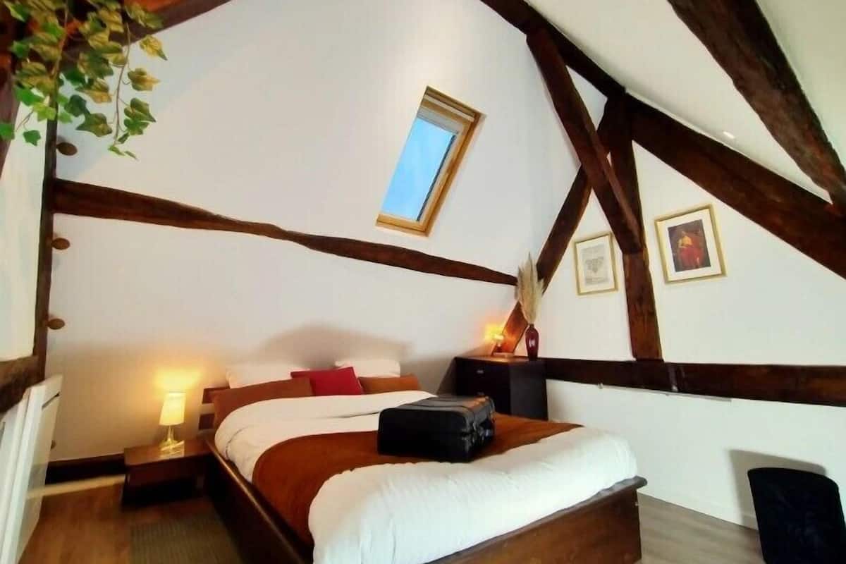 A bedroom with a bed, bedside lamps, a window, and wooden beams.