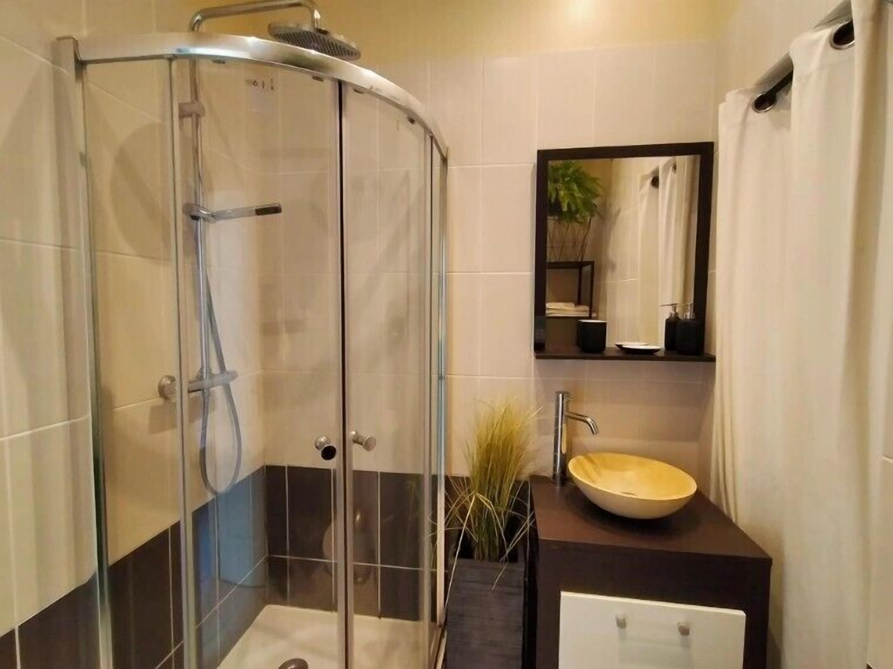 A modern bathroom with a glass-enclosed shower, a sink with a dark countertop, and a mirror above the sink.
