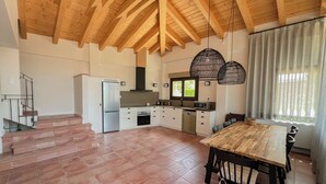 Una cocina amplia con techo de madera, un comedor con mesa y sillas de madera, y vista a un jardín por una ventana.
