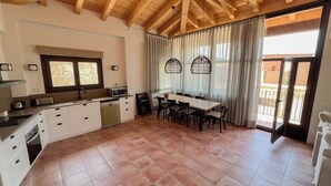 Una cocina amplia con comedor, vigas de madera en el techo y un gran ventanal con cortinas.