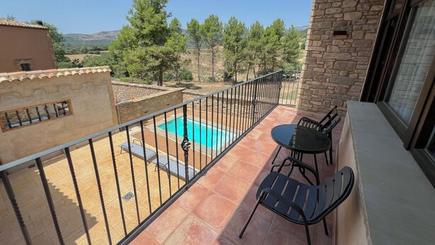 Un balcón con piscina, mobiliario exterior y vistas a árboles y colinas.