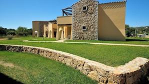 A modern building with a stone facade, multiple arches, and a well-maintained lawn. - Residenze del Mare (Porto Ottiolu)