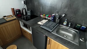 Une cuisine compacte dotée d’un plan de travail noir, d’un évier en acier inoxydable, de meubles en bois et d’un lave-vaisselle noir.