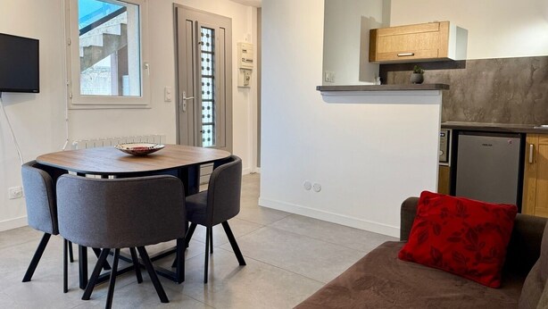 Une cuisine moderne dotée d’un réfrigérateur encastré, un coin repas avec une table ronde et des chaises, et un espace de vie chaleureux avec un canapé et un coussin rouge.
