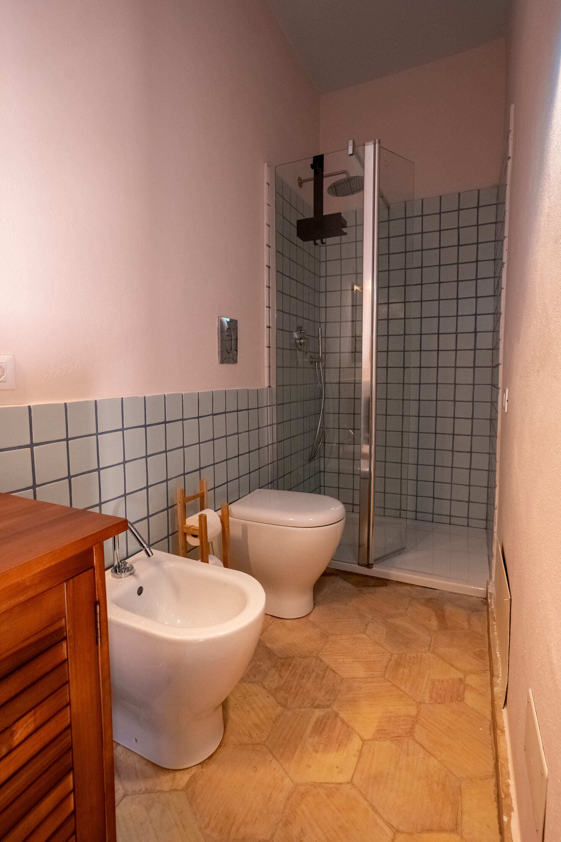 A bathroom with a shower, toilet, bidet, and wooden vanity.