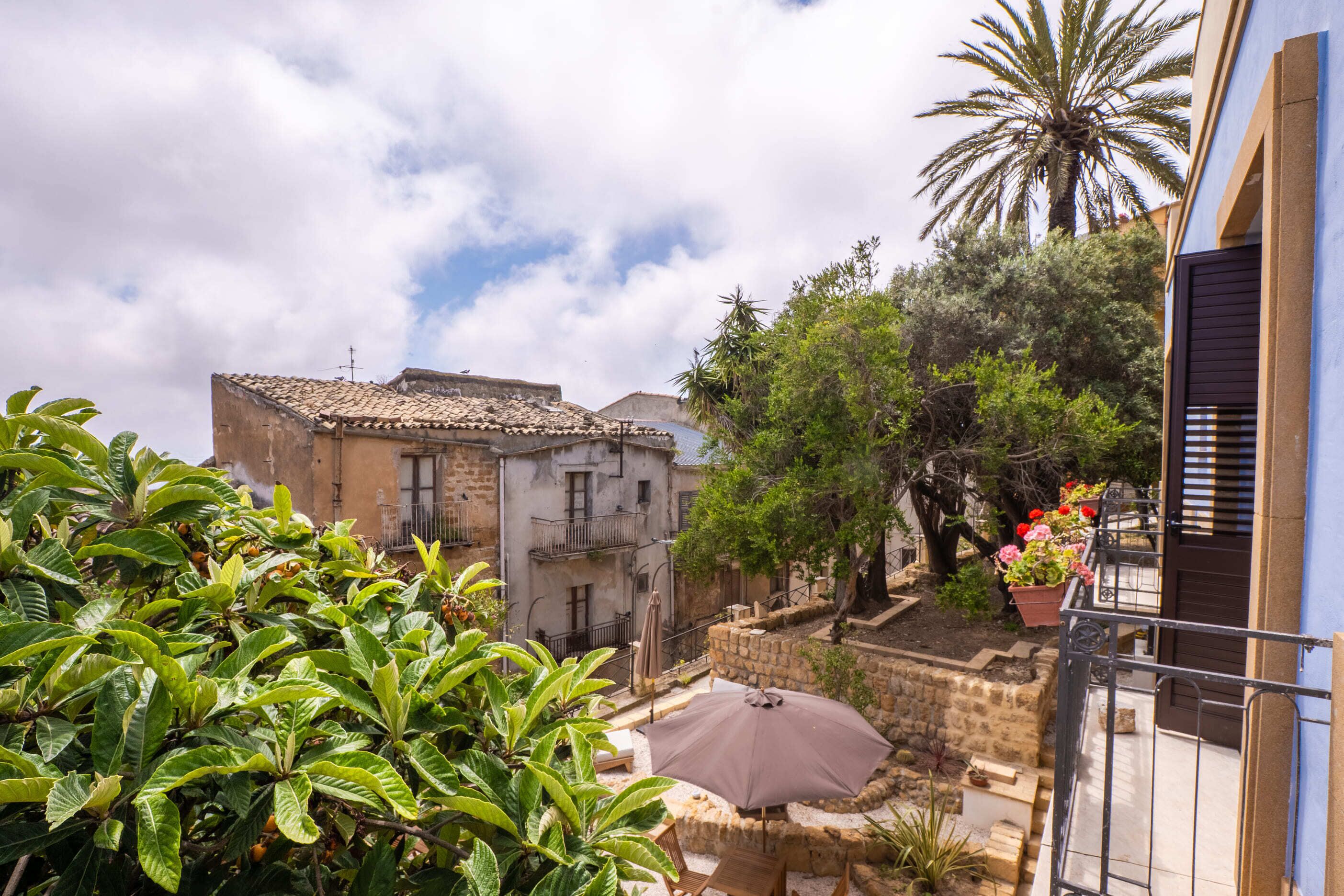 A courtyard with a tiled roof building, a palm tree, and potted plants.
