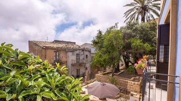 A courtyard with a tiled roof building, a palm tree, and potted plants.