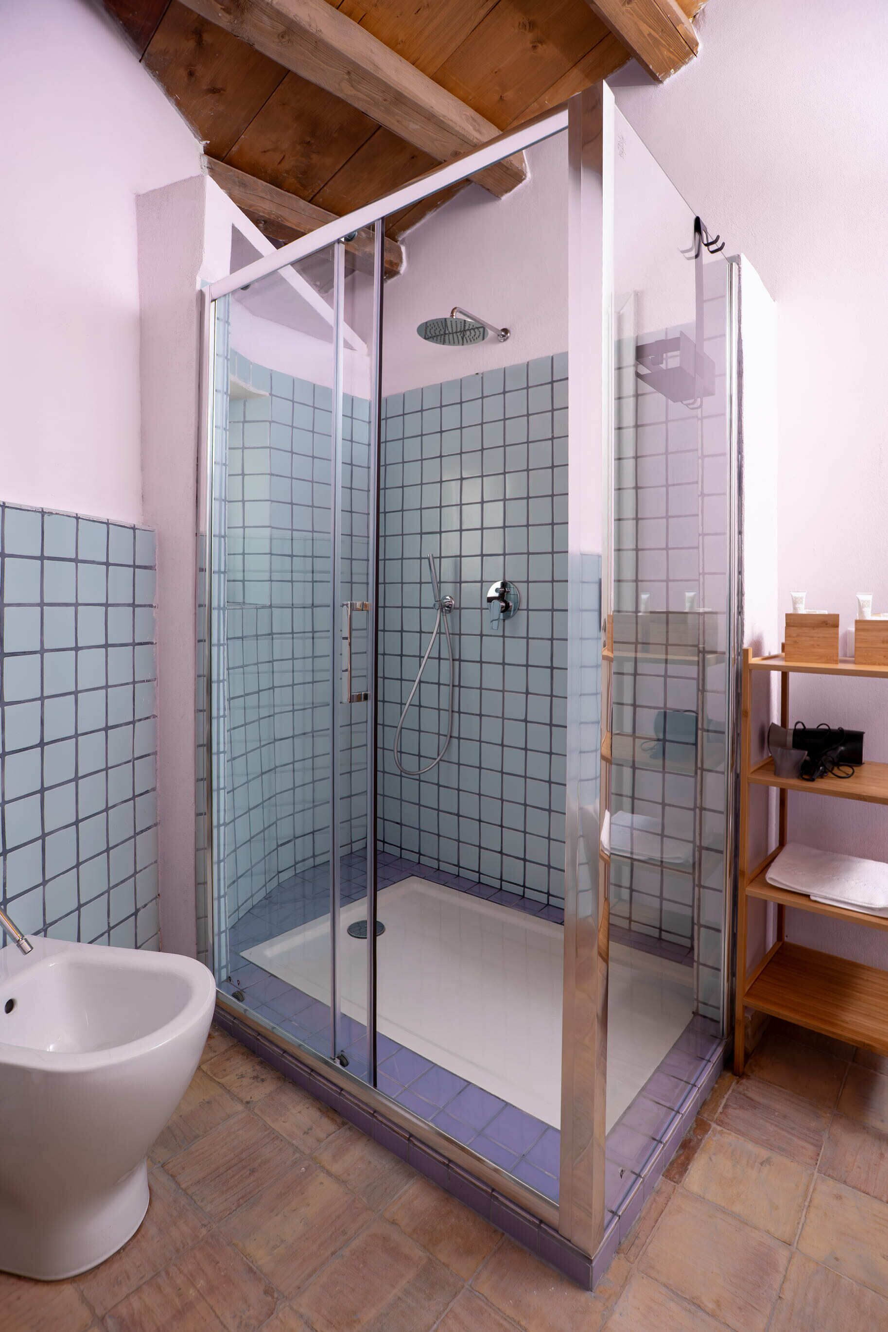 A modern bathroom with a glass-enclosed shower, a white toilet, and a wooden shelf with toiletries.