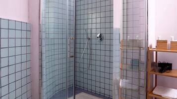 A modern bathroom with a glass-enclosed shower, a white toilet, and a wooden shelf with toiletries.