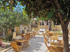 An outdoor seating area with wooden furniture and a stone wall in the background.